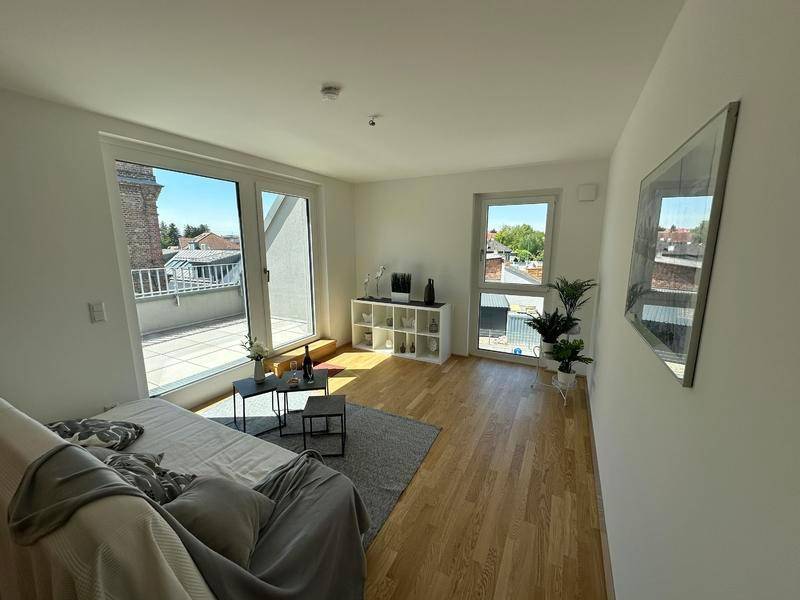 Helles Wohnzimmer mit Holzboden und großen Fenstern, die einen weiten Blick über die Dächer bieten.
