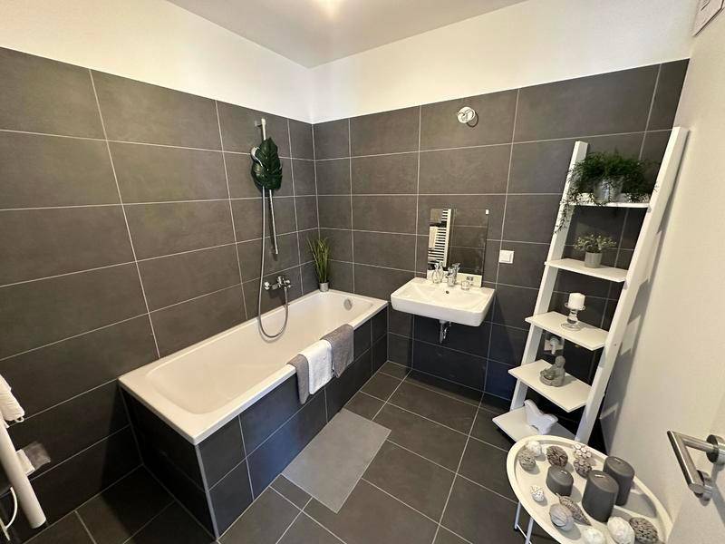 Modernes Badezimmer mit dunkelgrauen Fliesen, Badewanne mit Duschfunktion und einem einzelnen Waschbecken.