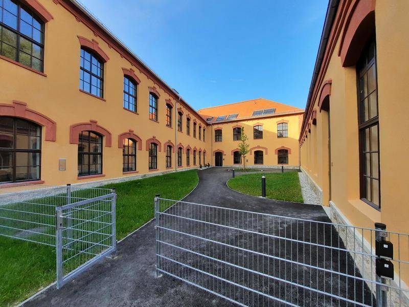 Innenhof des Gebäudes mit gepflegtem Rasen, Wegen und Zugang zu den Wohneinheiten.