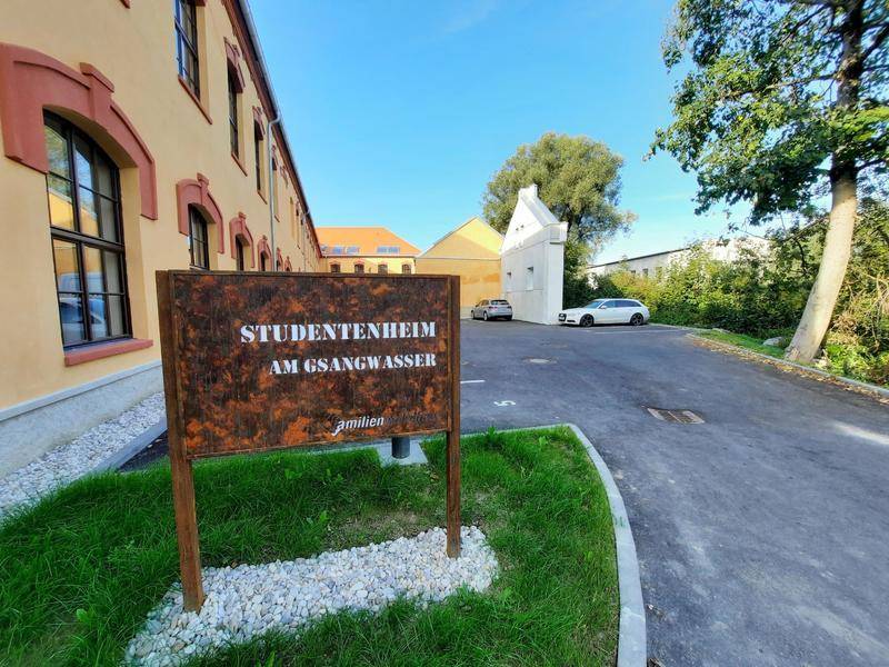 Eingangsbereich eines Studentenwohnheims mit Hinweisschild und Parkplätzen im Freien.
