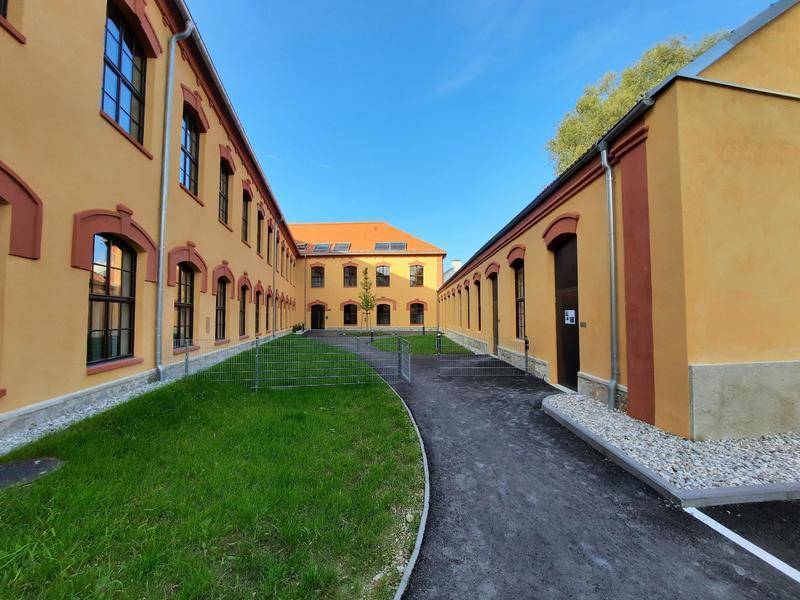Innenhof eines historischen Gebäudekomplexes mit gepflegter Grünfläche und Wegen unter blauem Himmel.