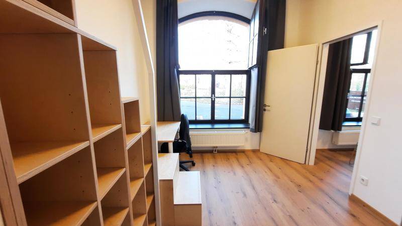 Helles Schlafzimmer mit Holzboden, großem Bogenfenster und integriertem Stauraum.