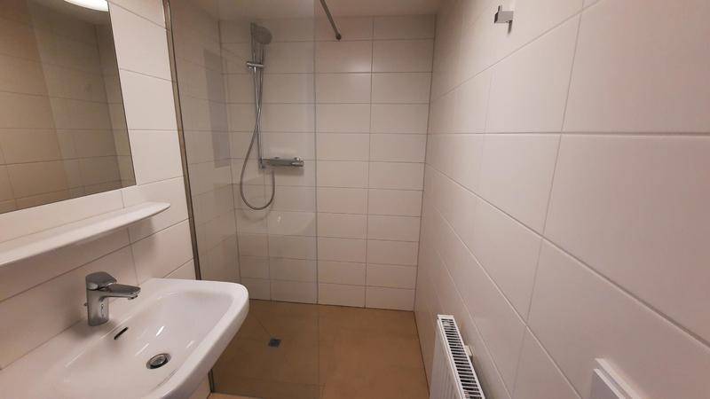 Funktionales Badezimmer mit ebenerdiger Dusche, Waschbecken und weißen Wandfliesen.