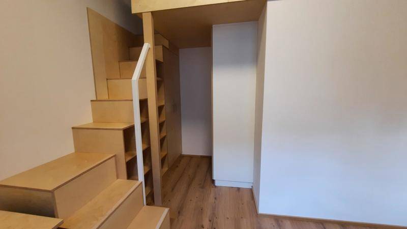 Holztreppe mit integrierten Regalen führt zur Schlafgalerie in einem modernen Raum.