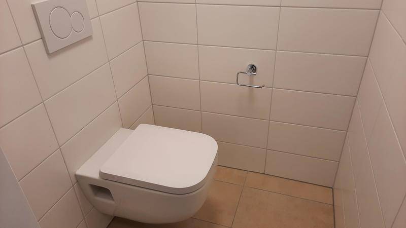Separates WC mit wandhängender Toilette und hellen Fliesen an Wänden und Boden.