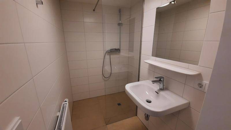 Modernes Badezimmer mit Duschkabine, Waschbecken und hellen Fliesen an Wänden und Boden.