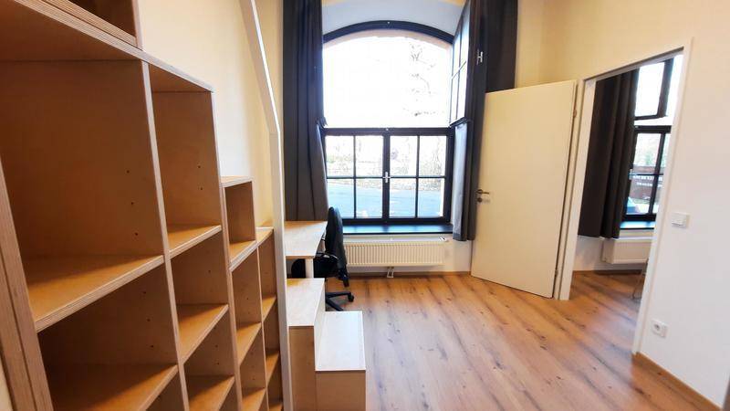 Heller Arbeitsbereich mit großem Bogenfenster und Holzregalen unter der Schlafgalerie.