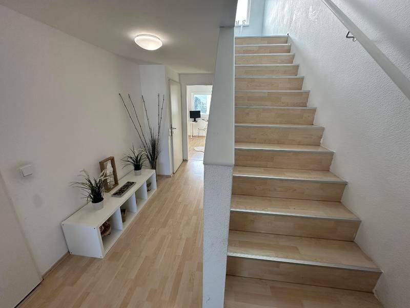 Heller Flur mit Holztreppe, die zu den oberen Etagen führt, und Laminatboden.