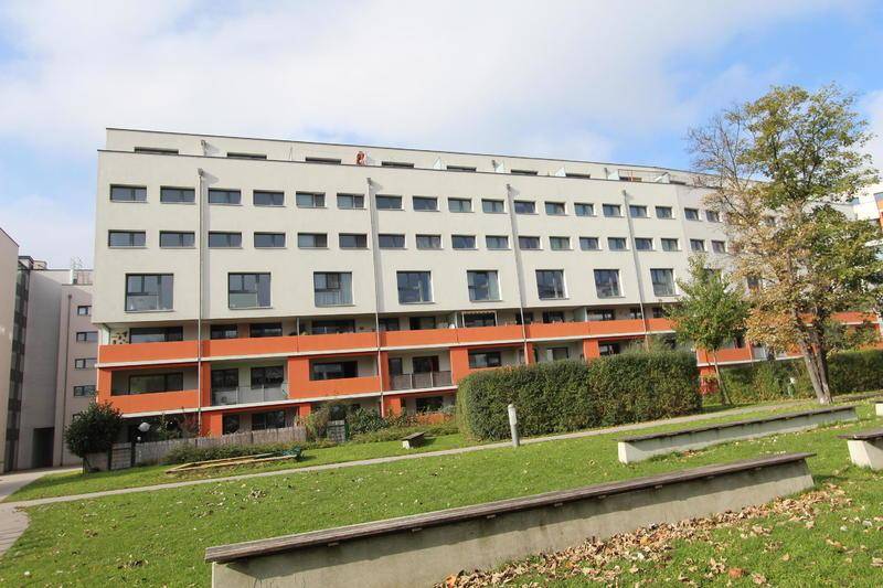 Moderne Wohnanlage mit weißer und oranger Fassade, umgeben von Grünflächen.