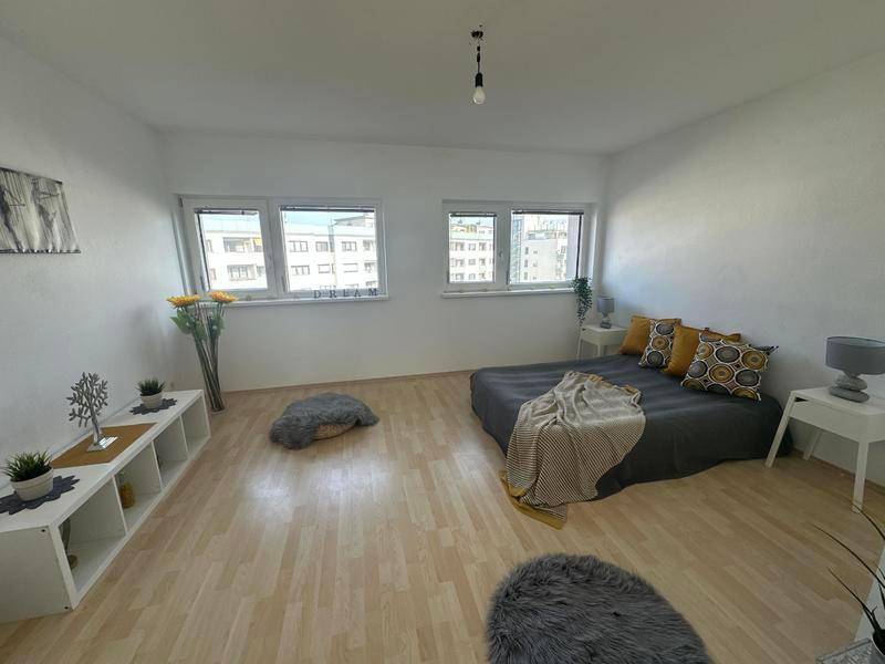 Geräumiges Schlafzimmer mit hellem Laminatboden, großen Fenstern und einfacher Einrichtung.
