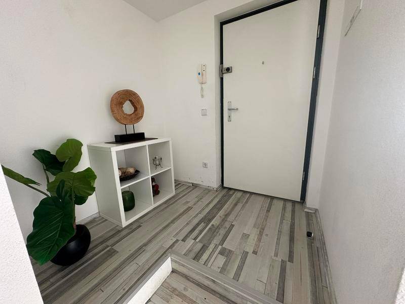 Eingangsbereich mit weißer Wohnungstür, Gegensprechanlage und dekorativem Regal.