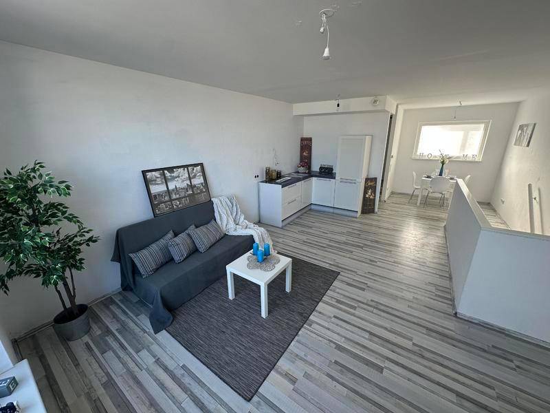 Helles Wohnzimmer mit integrierter Küchenzeile, Essbereich und modernem Laminatboden.