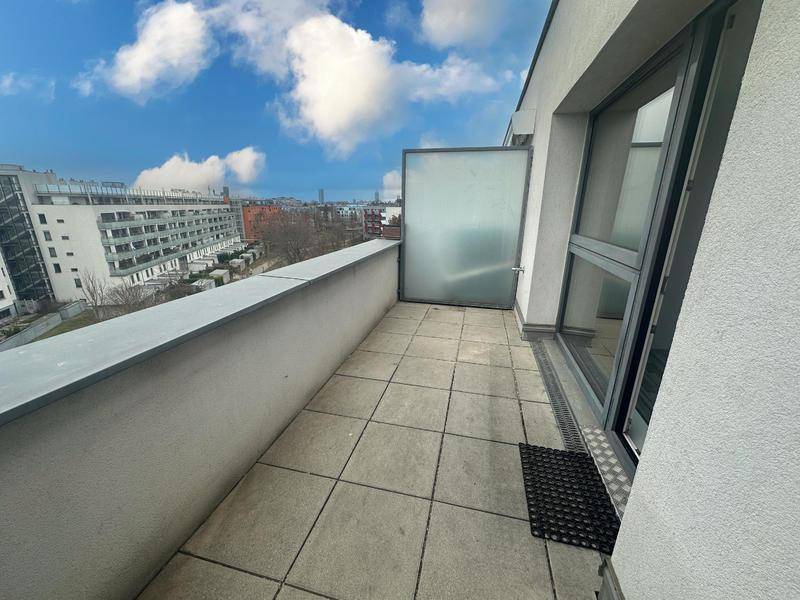 Geräumiger Balkon mit Fliesenboden und Blick auf die umliegenden Gebäude und den Himmel.