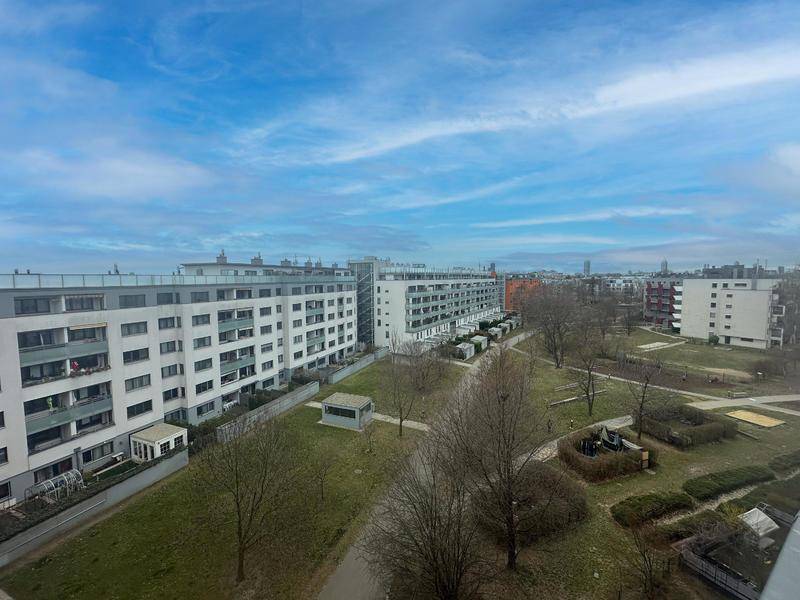 Weitläufiger Blick über die Wohnanlage mit Grünflächen und weiteren Gebäuden unter blauem Himmel.