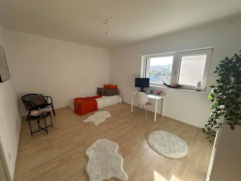 Freundliches Zimmer mit Tagesbett, Schreibtisch und Blick ins Grüne durch das Fenster.