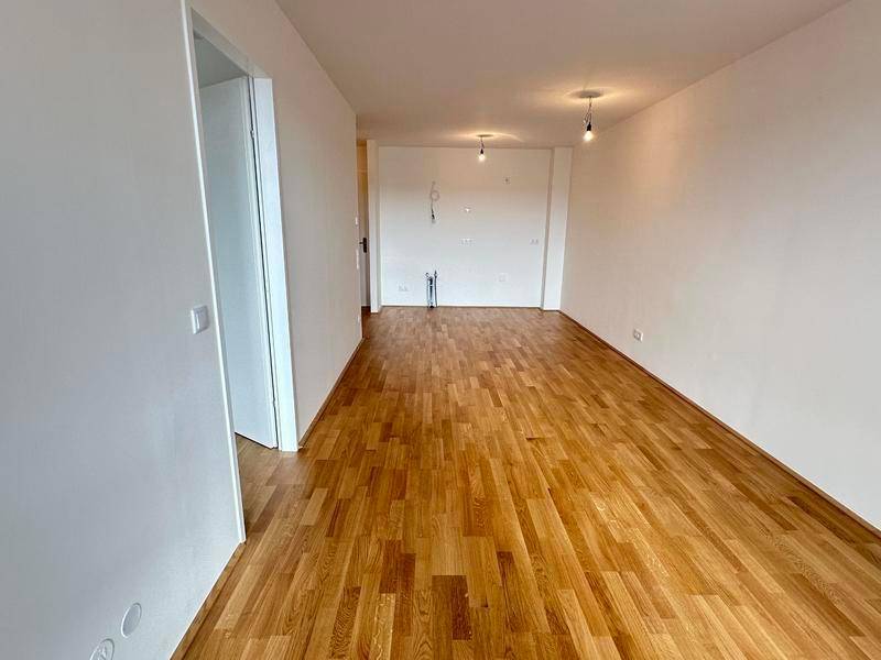 Leerer Wohnbereich mit hellem Holzboden und weißen Wänden, bereit zur individuellen Gestaltung.