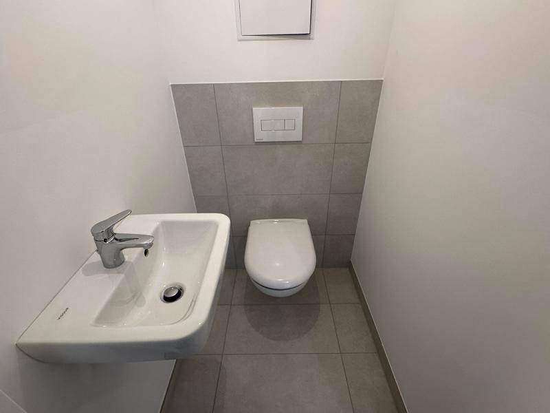 Modernes Gäste-WC mit Wand-WC, kleinem Waschbecken und grauen Wand- und Bodenfliesen.