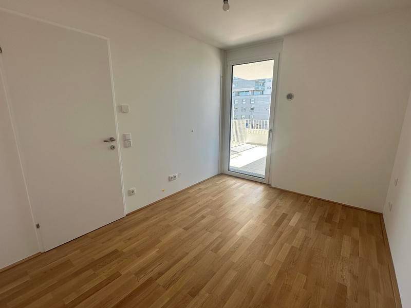 Helles Schlafzimmer mit Holzboden und Zugang zu einem kleinen Balkon oder einer Terrasse.
