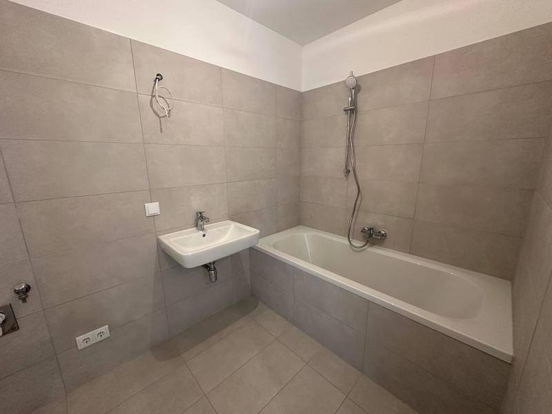 Modernes Badezimmer mit Badewanne, Waschbecken und grauen Wand- und Bodenfliesen.