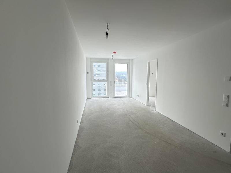 Leerer Raum mit weißen Wänden und Betonboden, bereit für den Ausbau und die individuelle Gestaltung.