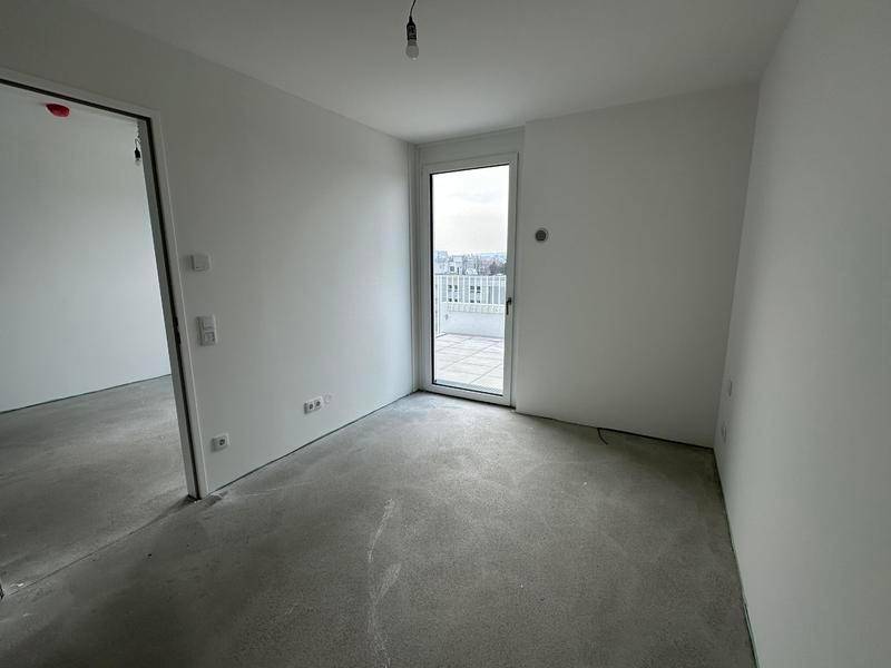 Heller, unmöblierter Raum mit Zugang zu einer Außenterrasse und sichtbarem Betonboden.