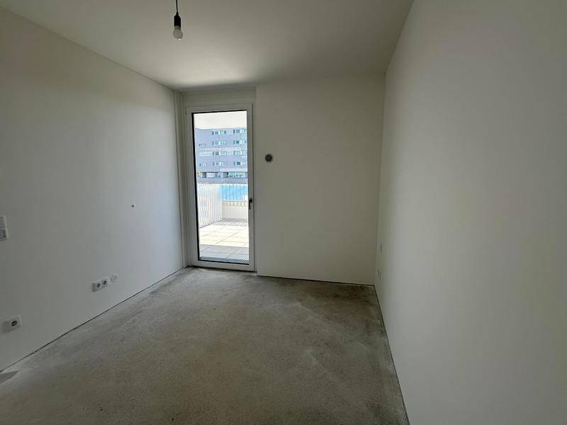 Leeres Schlafzimmer mit weiß gestrichenen Wänden, Betonboden und direktem Zugang zu einem Balkon.