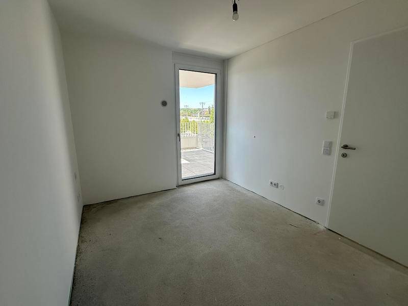 Helles Schlafzimmer mit Zugang zur Terrasse und unfertigem Bodenbelag.