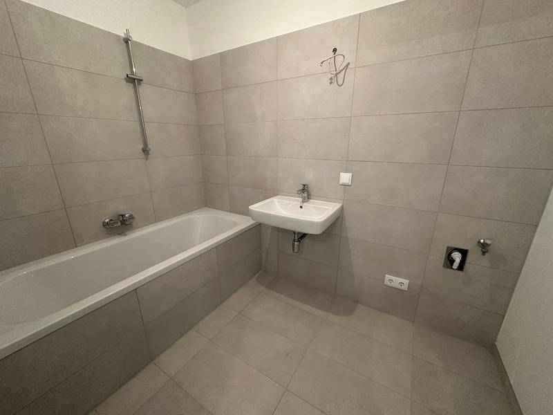 Modernes Badezimmer mit Badewanne, Waschbecken und hellgrauen Fliesen. Funktional und pflegeleicht gestaltet.