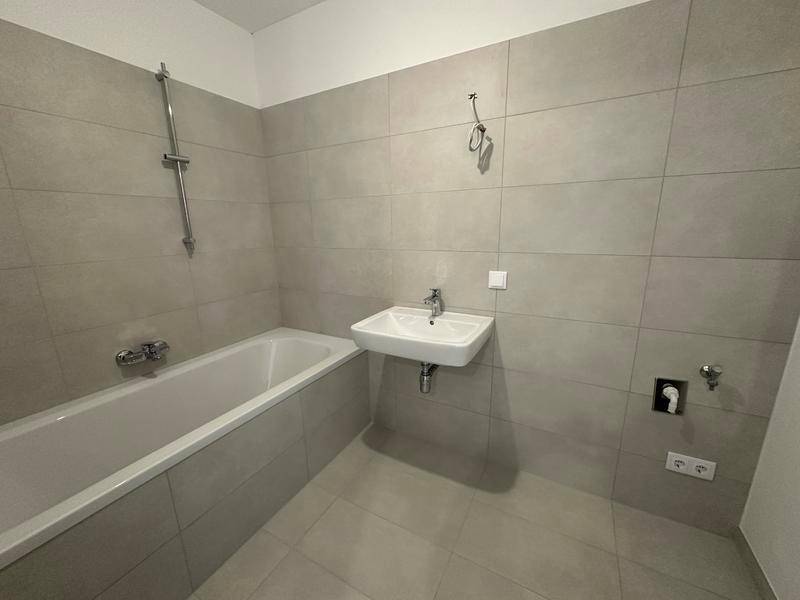Modernes Badezimmer mit grauen Fliesen, Badewanne und Einzelwaschbecken.