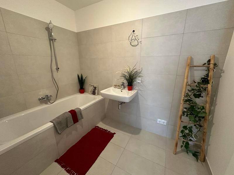 Modernes Badezimmer mit Badewanne, Waschbecken und hellen Fliesen an Wänden und Boden.