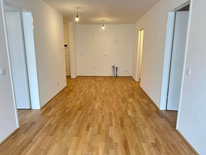Heller Raum mit Holzboden und Anschlüssen für eine zukünftige Küche.