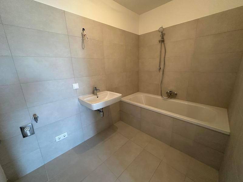 Modernes Badezimmer mit hellgrauen Fliesen, Badewanne und Einzelwaschbecken.
