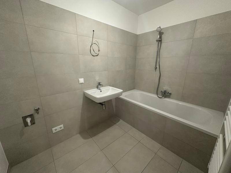 Modernes Badezimmer mit hellgrauen Fliesen, Badewanne und Waschbecken.