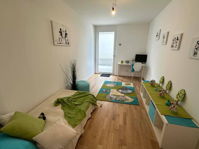 Kinderzimmer mit Holzboden, Schreibtisch und Zugang zu einem Außenbereich.