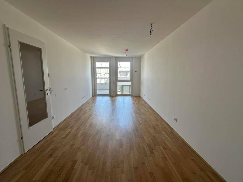 Heller, leerer Raum mit Holzboden und Zugang zu einem Balkon oder einer Terrasse.