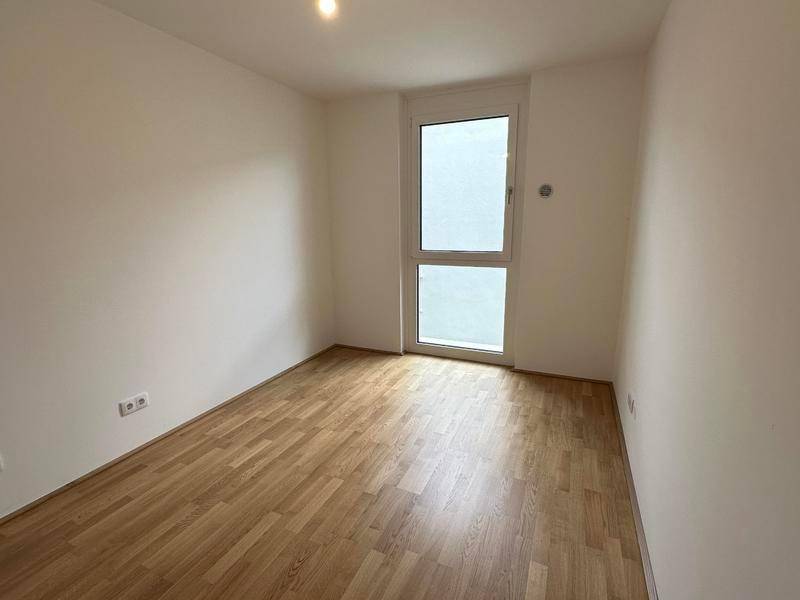 Helles Zimmer mit Holzboden und großem Fenster, ideal als Schlaf- oder Arbeitszimmer.