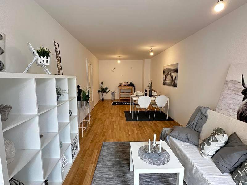 Offener Wohn- und Essbereich mit Holzboden, modernem Regal und gemütlicher Sitzecke.