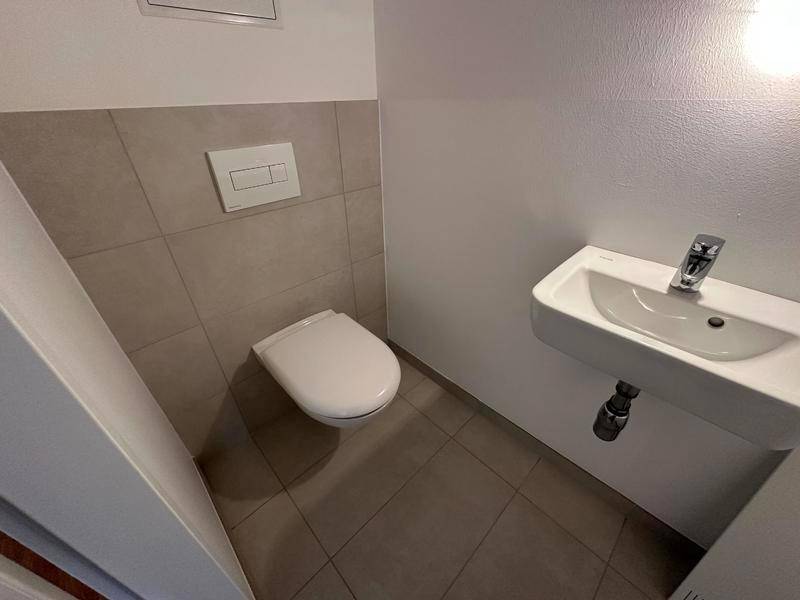 Gäste-WC mit wandhängender Toilette, Einzelwaschbecken und modernen Fliesen.