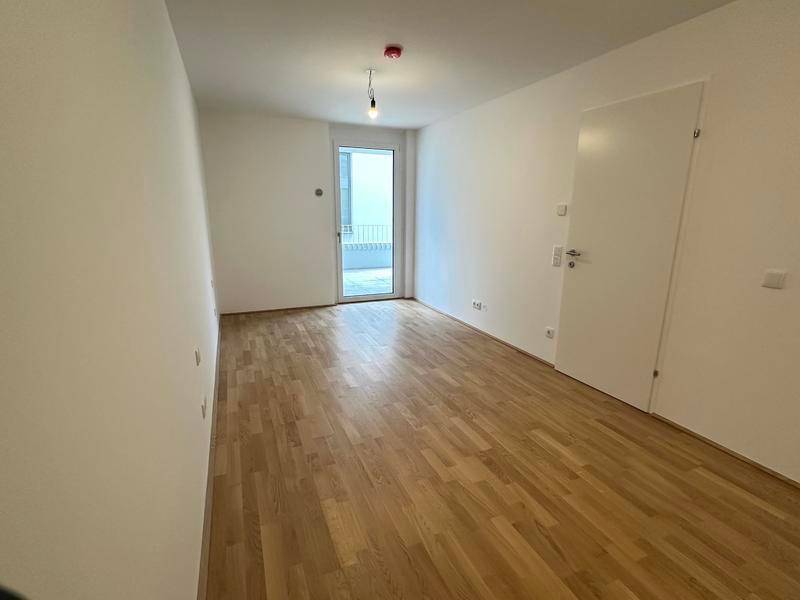 Leeres Zimmer mit Holzboden und Zugang zu einem Außenbereich.