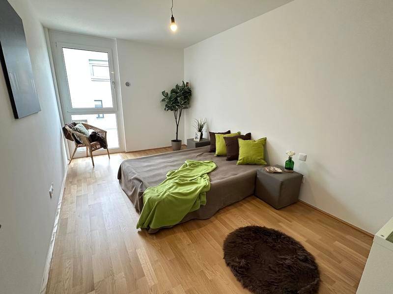 Schlafzimmer mit Holzboden, großem Fenster und einem bequemen Bett mit grünen Kissen.
