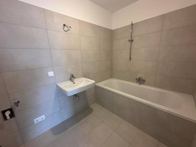Modernes Badezimmer mit hellgrauen Fliesen, einer Badewanne und einem wandmontierten Waschbecken.