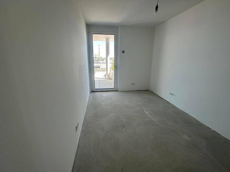 Helles Zimmer mit weißen Wänden, Betonboden und direktem Zugang zu einem Außenbereich.