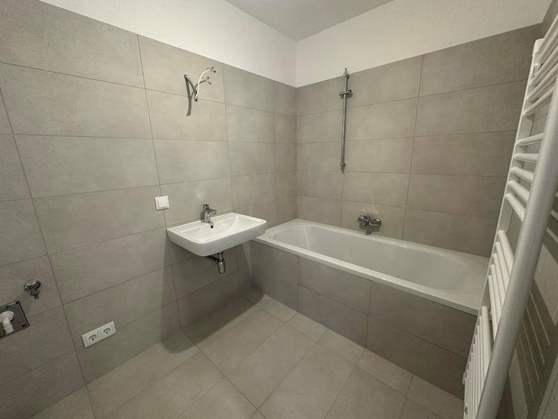 Modernes Badezimmer mit grauen Fliesen, Badewanne mit Duschfunktion und beheiztem Handtuchhalter.