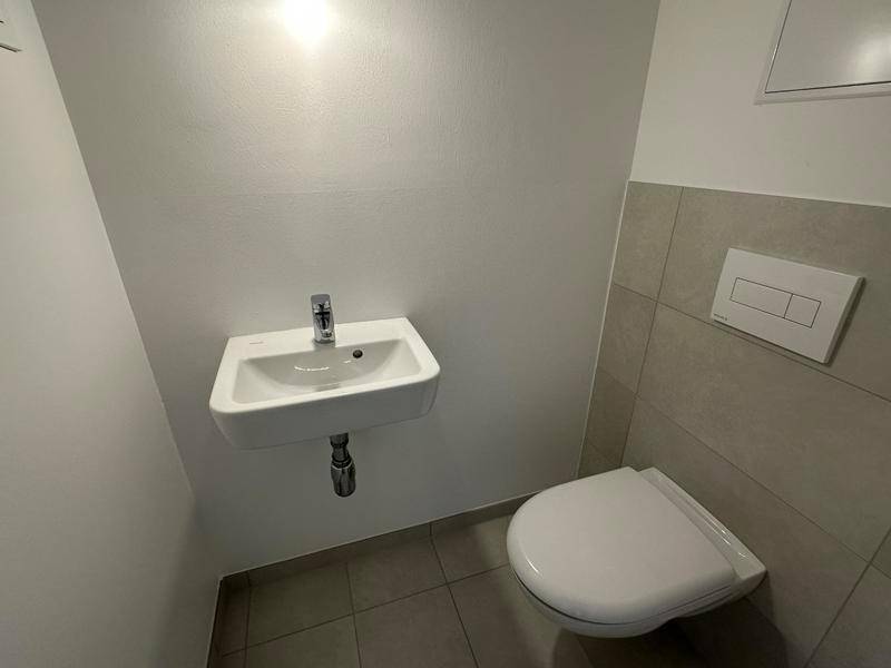 Funktionelles Gäste-WC mit hellgrauen Fliesen, wandhängendem WC und kleinem Waschbecken.