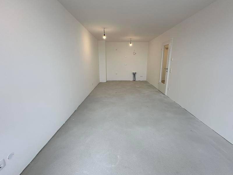 Leerer Raum mit weißen Wänden, Betonboden und Anschlüssen für eine zukünftige Küche.