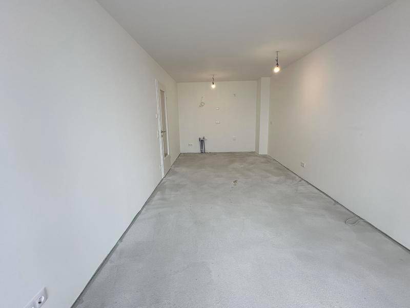 Leerer Küchenraum mit weißen Wänden, Betonboden und vorbereiteten Anschlüssen für eine Einbauküche.