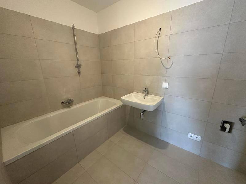 Modernes Badezimmer mit hellgrauen Fliesen, einer Badewanne und einem einzelnen Waschbecken.
