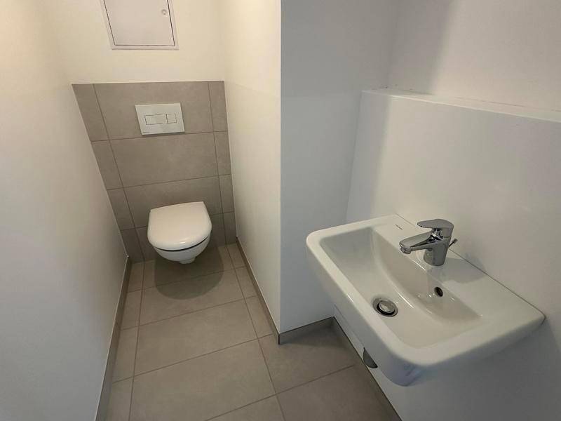 Separates Gäste-WC mit wandhängender Toilette und kleinem Waschbecken, komplett gefliest.