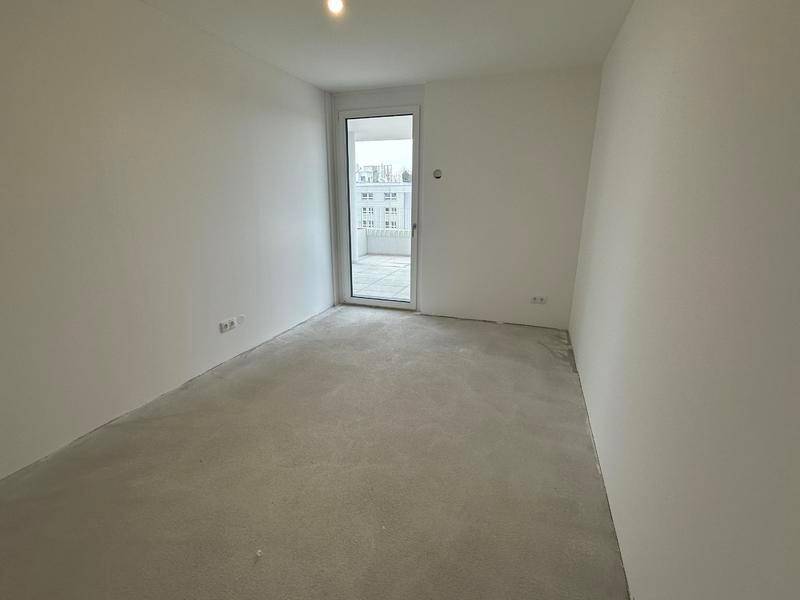 Helles Schlafzimmer mit Zugang zum Balkon, weißen Wänden und Betonboden, bereit zur Einrichtung.