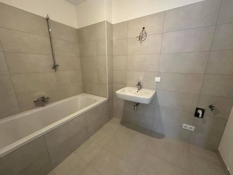 Modernes Badezimmer mit hellgrauen Fliesen, Badewanne mit Duschfunktion und einem einzelnen Waschbecken.